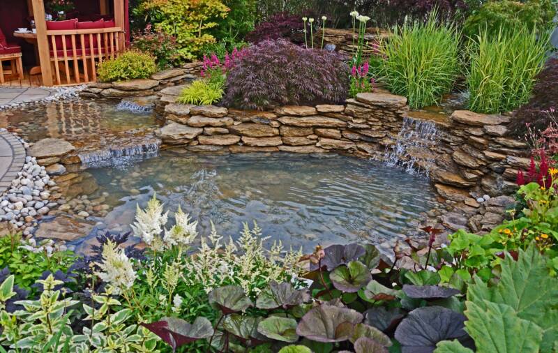 The pond in an aquatic garden with planted rockery and waterfalls and summer house