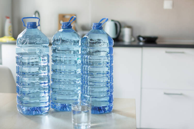 Big plastic bottle with water on the table over bright kitchen backgroung. Bottle of clear transarent water in a blue color cap and handle closeup